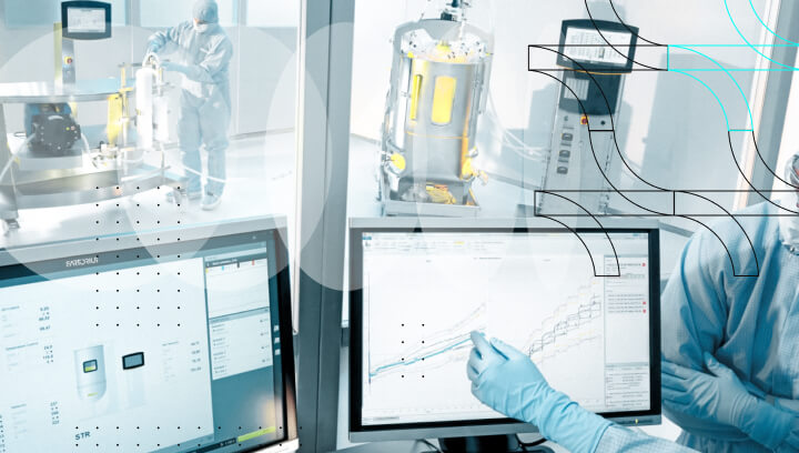 GMP cleanroom scientist reviewing real-time PAT process data on dual monitors with bioreactor equipment in background.